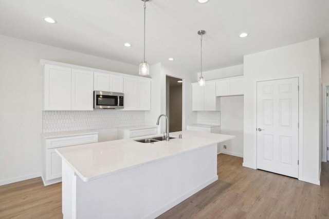 kitchen featuring white cabinets, a center island with sink, stainless steel microwave, and light countertops