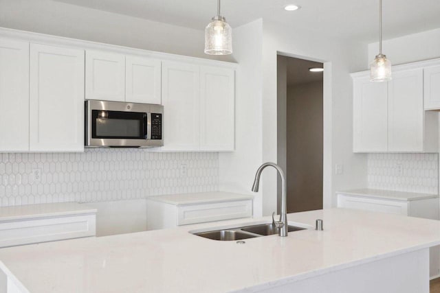 kitchen with light countertops, stainless steel microwave, decorative light fixtures, and white cabinetry