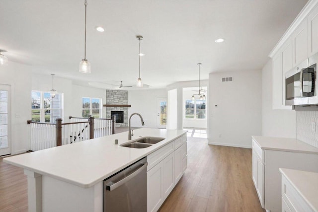 kitchen with stainless steel appliances, light countertops, open floor plan, a kitchen island with sink, and a sink