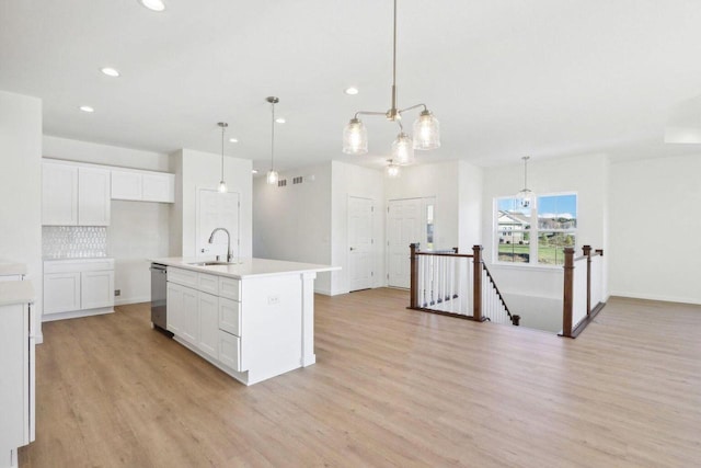 kitchen with white cabinets, light countertops, a center island with sink, and decorative light fixtures