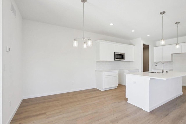 kitchen featuring light countertops, stainless steel microwave, a kitchen island with sink, and white cabinetry