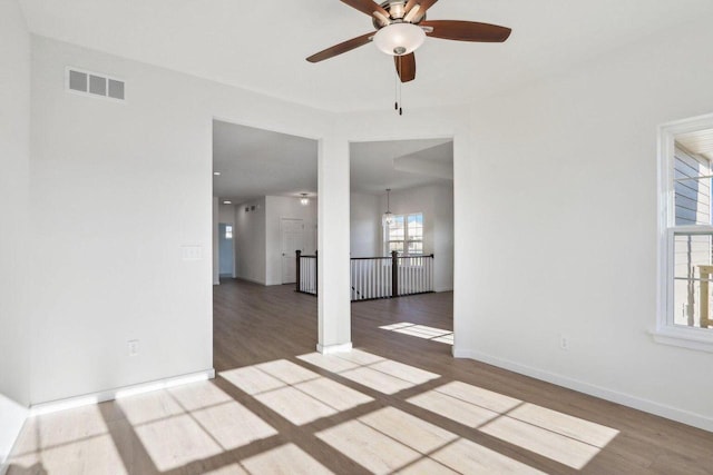 empty room with ceiling fan, wood finished floors, visible vents, and baseboards