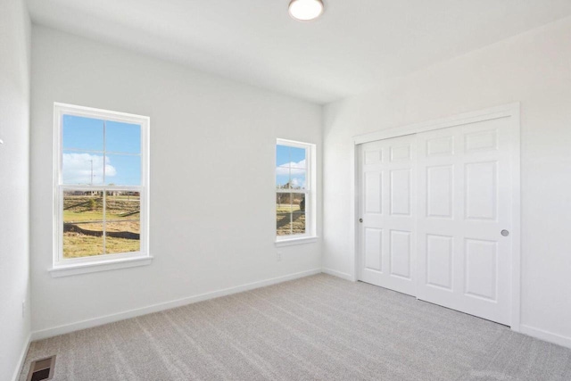 unfurnished bedroom featuring baseboards, a closet, visible vents, and light colored carpet