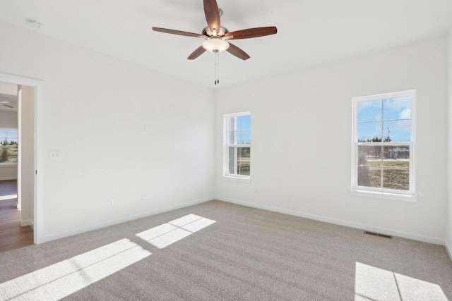 spare room with light colored carpet, visible vents, ceiling fan, and baseboards