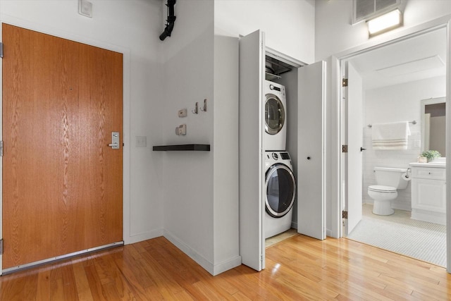 washroom with stacked washing maching and dryer, visible vents, laundry area, and light wood-style flooring