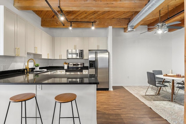 kitchen with a peninsula, stainless steel appliances, a kitchen bar, white cabinetry, and a sink