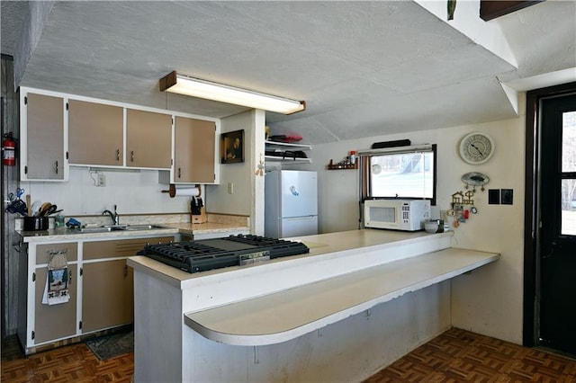 kitchen featuring a textured ceiling, a peninsula, white appliances, a sink, and light countertops