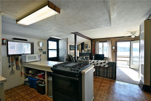 kitchen with a textured ceiling, white microwave, a ceiling fan, open floor plan, and black range with gas stovetop