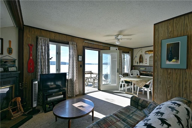 carpeted living room featuring a textured ceiling, ceiling fan, wood walls, and a glass covered fireplace