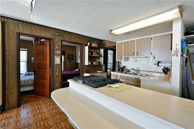 kitchen with a textured ceiling, light countertops, wood walls, and a sink