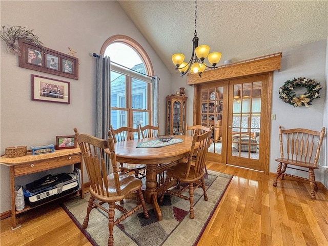 dining room featuring a textured ceiling, light wood-style floors, vaulted ceiling, french doors, and an inviting chandelier