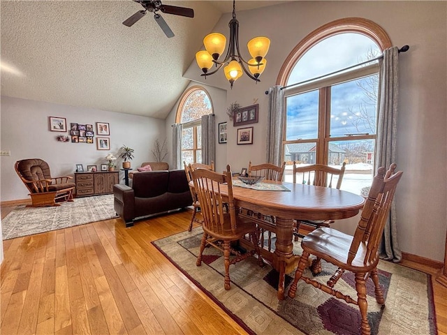 dining area featuring light wood finished floors, baseboards, vaulted ceiling, a textured ceiling, and ceiling fan with notable chandelier