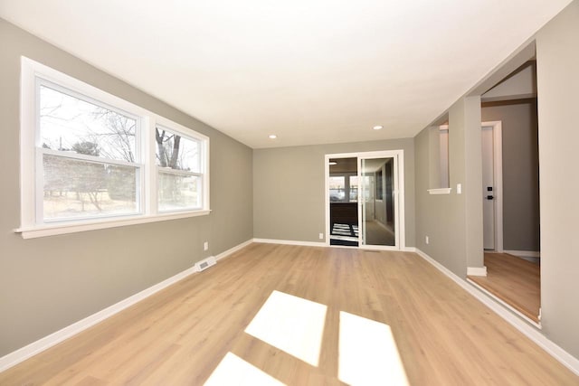 spare room featuring a healthy amount of sunlight, visible vents, light wood-style flooring, and baseboards