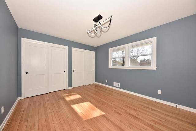 unfurnished bedroom with multiple closets, visible vents, light wood-style flooring, and baseboards