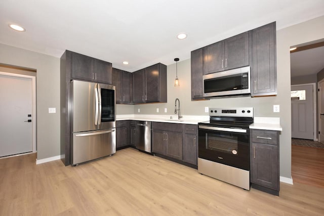 kitchen with light wood-style flooring, stainless steel appliances, a sink, light countertops, and decorative light fixtures