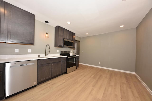 kitchen with dark brown cabinetry, hanging light fixtures, stainless steel appliances, light countertops, and a sink