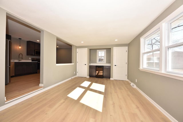 unfurnished living room featuring visible vents, a sink, light wood finished floors, and baseboards