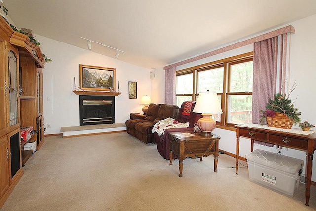 living room featuring carpet, lofted ceiling, rail lighting, a glass covered fireplace, and baseboards