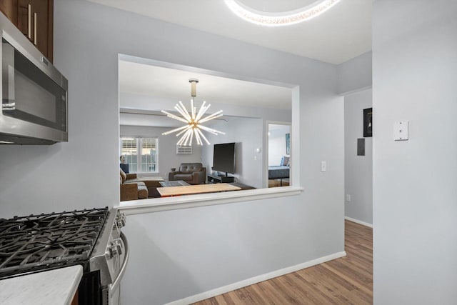 kitchen featuring a chandelier, dark brown cabinetry, stainless steel appliances, wood finished floors, and baseboards