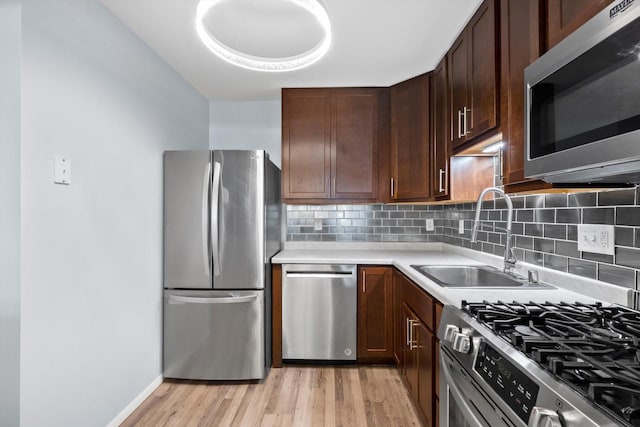 kitchen featuring appliances with stainless steel finishes, a sink, light countertops, light wood-style floors, and backsplash