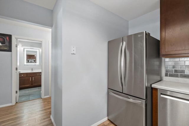 kitchen featuring light wood finished floors, tasteful backsplash, light countertops, appliances with stainless steel finishes, and baseboards