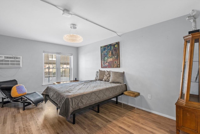 bedroom with a wall unit AC, wood finished floors, and baseboards