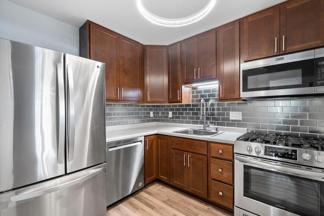 kitchen featuring stainless steel appliances, light countertops, backsplash, light wood-style floors, and a sink