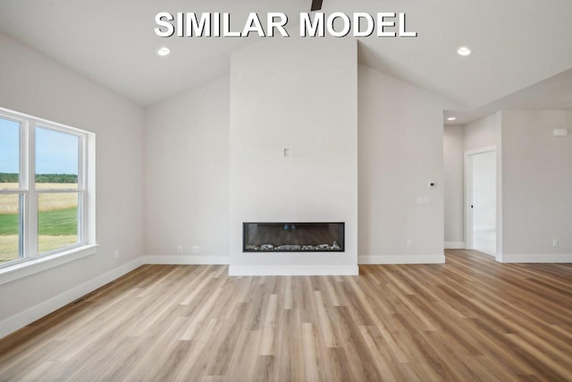 unfurnished living room with lofted ceiling, baseboards, wood finished floors, and a glass covered fireplace