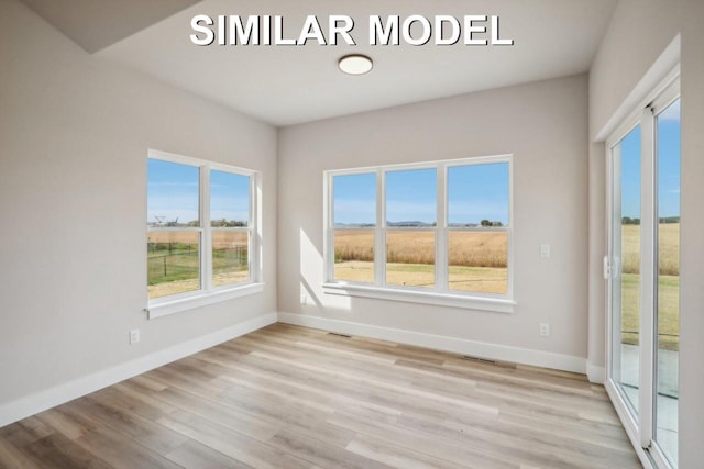 spare room with a rural view, wood finished floors, and baseboards