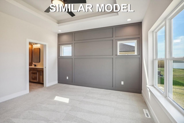 unfurnished bedroom featuring a raised ceiling, light colored carpet, a decorative wall, visible vents, and baseboards