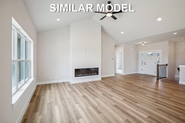 unfurnished living room featuring baseboards, a glass covered fireplace, light wood-style floors, high vaulted ceiling, and recessed lighting