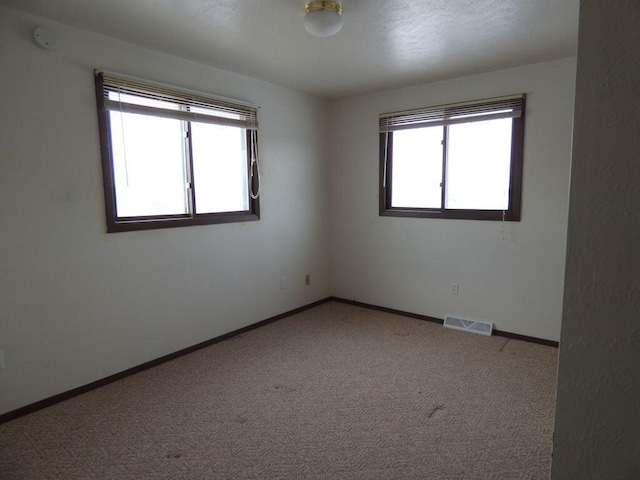 spare room with carpet flooring, visible vents, and baseboards