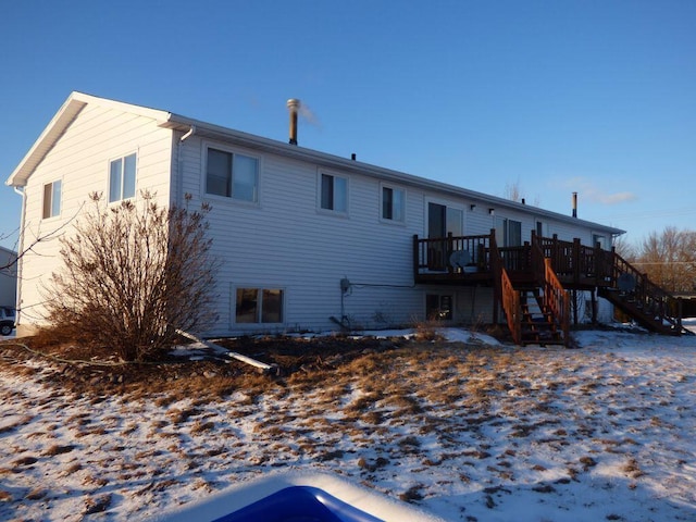 snow covered back of property with stairs and a deck