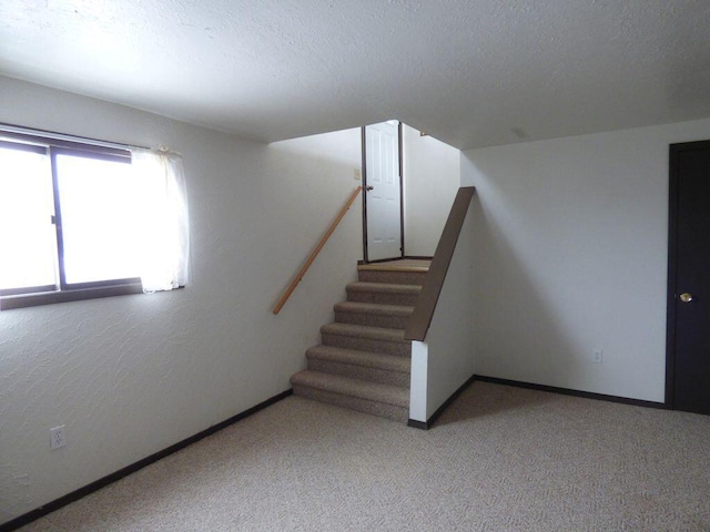 spare room with carpet floors, baseboards, stairway, and a textured ceiling