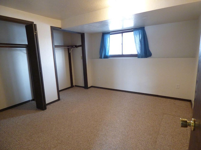 unfurnished bedroom with two closets, light colored carpet, and baseboards