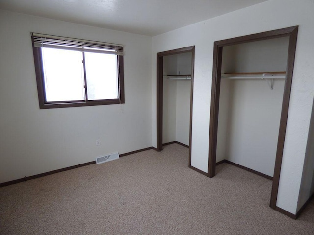 unfurnished bedroom featuring light carpet, two closets, visible vents, and baseboards