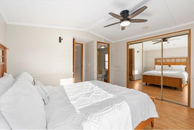 bedroom featuring lofted ceiling, a closet, ornamental molding, wainscoting, and light wood-type flooring