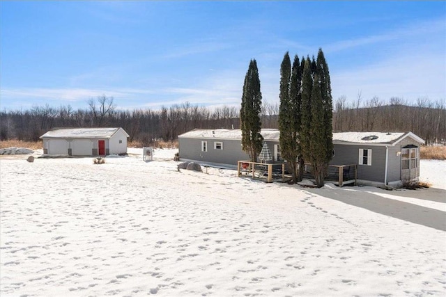 snow covered rear of property featuring a garage and an outbuilding