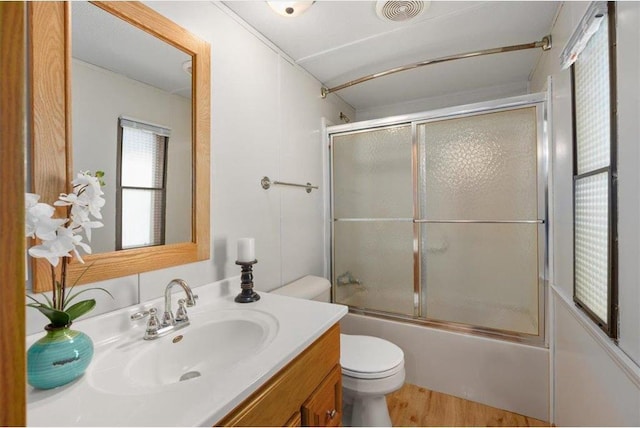 bathroom with visible vents, bath / shower combo with glass door, toilet, wood finished floors, and vanity