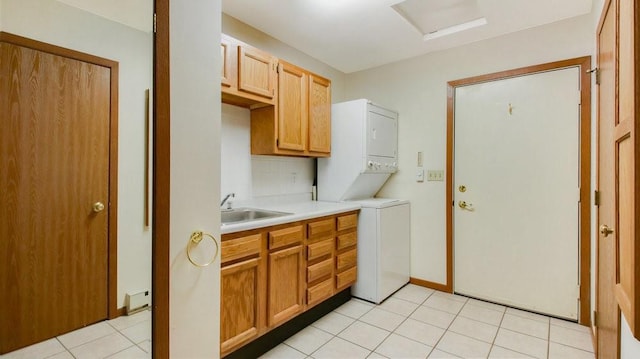 clothes washing area featuring stacked washer and clothes dryer, cabinet space, light tile patterned flooring, a sink, and baseboards