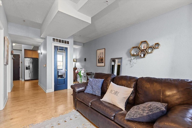 living room featuring light wood-type flooring, baseboards, and a textured ceiling