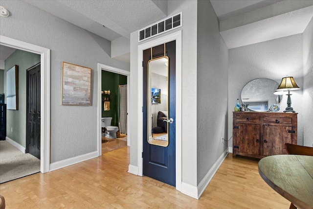 hallway with light wood finished floors, baseboards, visible vents, and a textured wall