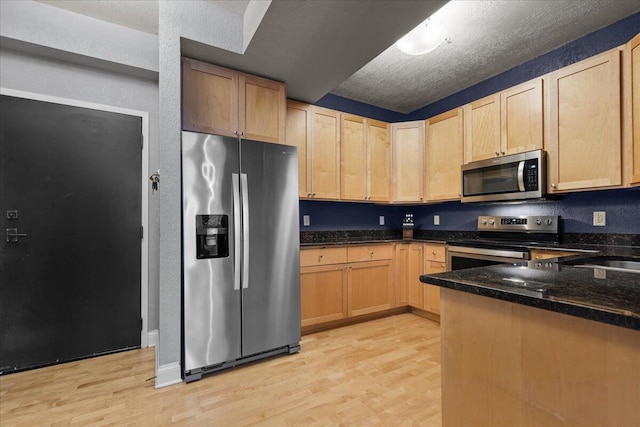 kitchen with stainless steel appliances, light wood-style floors, light brown cabinets, a textured ceiling, and dark stone countertops