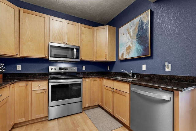 kitchen with a textured ceiling, light wood-style flooring, a sink, appliances with stainless steel finishes, and light brown cabinetry