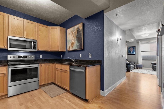 kitchen featuring a textured ceiling, a textured wall, light wood-style flooring, a sink, and appliances with stainless steel finishes