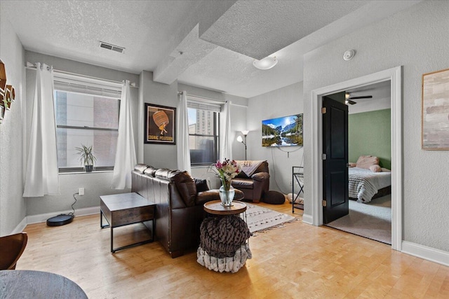 living area with visible vents, a textured wall, a textured ceiling, and baseboards