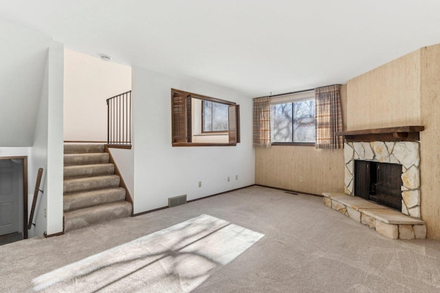 unfurnished living room featuring visible vents, carpet flooring, a stone fireplace, and stairs