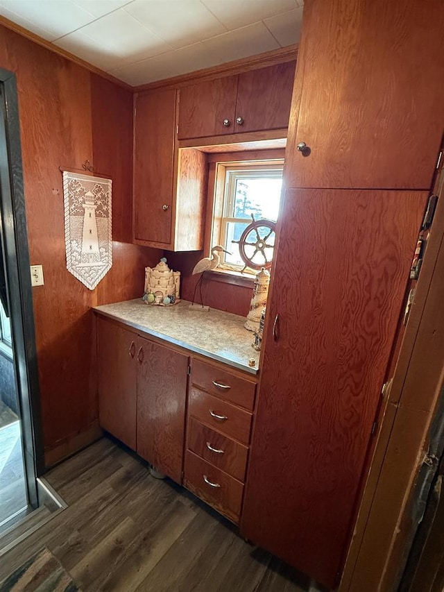 kitchen with dark wood-style floors, light countertops, wooden walls, and brown cabinets