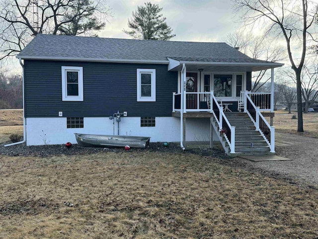 view of front of home with covered porch, roof with shingles, a front yard, and stairs