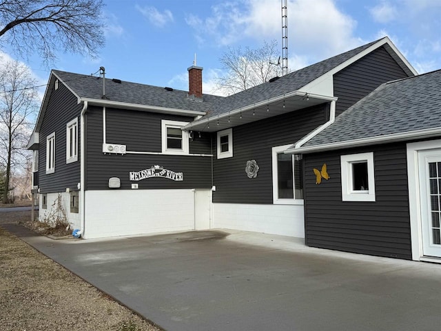 exterior space with driveway, a shingled roof, and a chimney